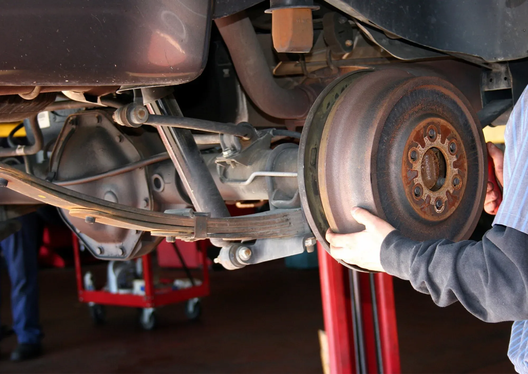 A Tiremaxx technician servicing a vehicle's brakes on the lift